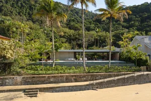A minimalist house with concrete walls and a large glass wall, surrounded by lush greenery.