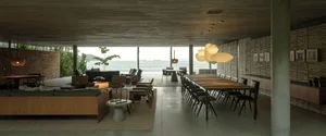 Modern, open-plan living room with concrete walls and floor, large windows overlooking the sea, and ergonomic furniture.