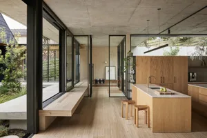 A modern kitchen with wooden cabinets and open shelving, featuring a large window and a concrete floor.