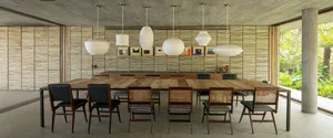 A modern living room features a wooden dining table surrounded by black and white patterned chairs. The room has a concrete c