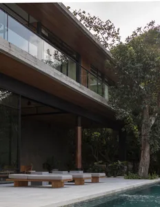 A modern residential exterior featuring a concrete and wooden structure, with a glass wall and a pool in the foreground.