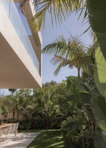 Modern residential exterior with glass walls and concrete facade, surrounded by lush greenery.