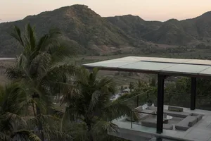 Modern residential terrace with concrete and glass structures surrounded by palm trees, overlooking scenic mountainous landsc