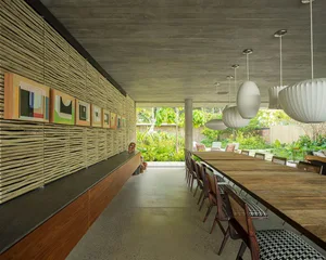 A modern restaurant interior featuring wooden tables, concrete walls, and plants.