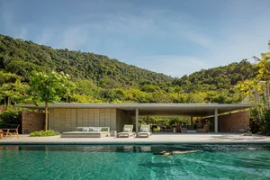 A modern poolside lounge area featuring a sleek, concrete platform, surrounded by lush greenery.