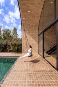Person swinging on a rope swing outside a modern house with brick tile flooring and glass walls.