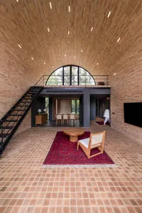 A modern living room with grey clay tiles on the floor and walls, featuring a large arched window and a wooden chair on a red