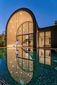 A modern minimalist house with a glass wall reflected in a swimming pool.