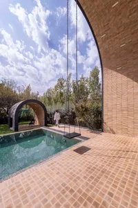 A modern swimming pool with tiled flooring and walls, featuring an outdoor swing and a covered seating area.