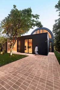 A modern residential house with a black exterior and large windows, surrounded by greenery.