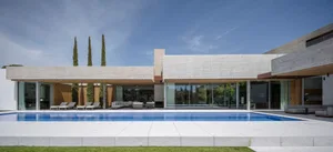 Modern residential exterior with a concrete facade and a swimming pool surrounded by a patio with an outdoor seating area.
