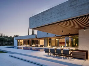 A modern residential villa featuring concrete exteriors and a pool with lounge seating.