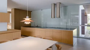 A modern kitchen featuring wood cabinetry, glass backsplash, and stainless steel appliances.
