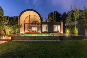 Modern residential architecture featuring an arched entrance and a swimming pool illuminated at night.