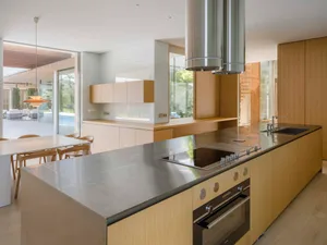 Modern, residential kitchen with wood cabinetry, stainless steel countertops, and glass backsplash.