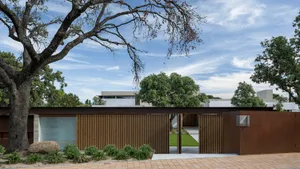 A modern residential exterior with a metal fence and rustic tree.