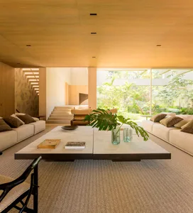 A modern living room with a wooden coffee table, white sofas, and large windows overlooking a garden.