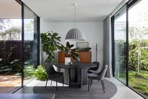 A modern dining room with a round black dining table, black upholstered chairs, a large green plant, and a round pendant ligh