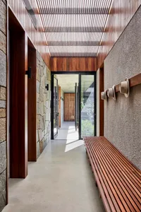 Interior design image showing a modern entrance hallway with wooden slat ceiling, concrete floor, stone accent wall, and wood