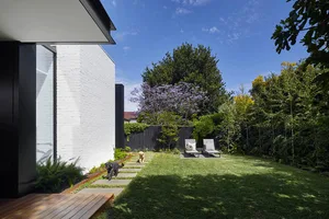 A modern house exterior with a concrete pathway and a brick wall in the backyard.