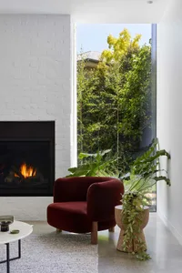 Modern living room featuring a fireplace, red armchair, and potted plants.