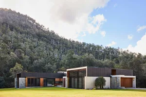 A modern residential exterior featuring wood, stone, and metal materials.
