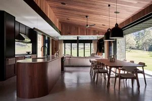 Modern residential interior with wooden furniture, large windows, and a spacious living area with a comfortable sofa and a di