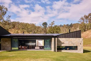 Modern residential building with stone and glass exterior, featuring expansive windows and a spacious outdoor area.