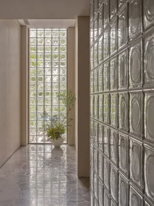 A glass block corridor with a vase of flowers on the floor in a well-lit space.