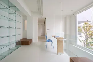 極簡辦公室室內，設有玻璃置物架、藍色座椅，以及窗外樹景。