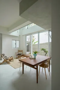 A minimalist interior featuring a modern dining room with wood furniture and a view of a bonsai tree through large windows.