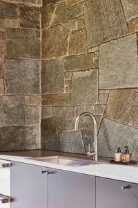 A modern kitchen with a stone wall and stainless steel faucet