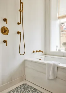 Modern minimalist bathroom with white walls, marble finishes, and brass fixtures.