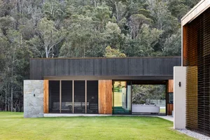 A modern residential exterior featuring wooden panels, glass doors, and stone accents.