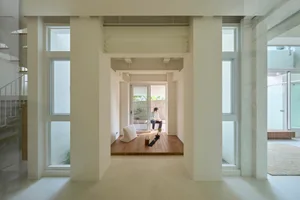 A minimalist interior space with white walls, wood flooring, and a concrete structure.