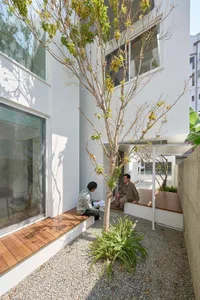 Minimalist residential outdoor space featuring concrete and wood materials, with two individuals sitting on benches surrounde