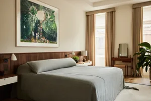 Modern bedroom featuring gray textiles, white accent blinds, and a large painting above the bed.