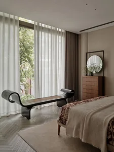 A modern bedroom with a bed, dresser, and bench, featuring wooden floors and fabric bedding.