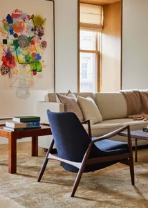 A contemporary living room with a blue sofa, wooden coffee table, abstract painting, and beige couch.
