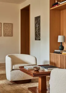 A modern living room featuring a comfortable fabric lounge chair, a wooden table with books, and a built-in bookshelf.