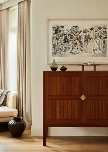 Modern living room featuring a wooden cabinet with artwork on the wall and a comfortable seating area by the window.