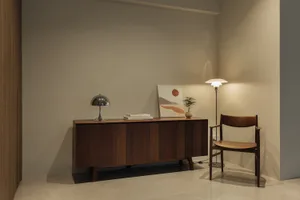A modern living room featuring wooden furniture, a wooden sideboard with books and a plant, and a floor lamp.