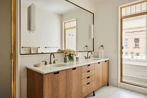 A modern bathroom featuring a marble countertop, oak cabinets, and brass fittings.