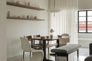 A modern minimalist dining room with a white dining table, chairs, and bench, white curtains, and wooden shelves.