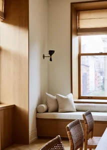 Modern residential space featuring comfortable seating with wooden cushions and a window with light filtering through blinds.