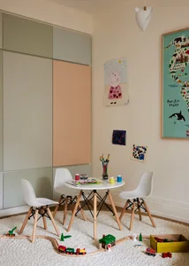 A modern playroom with wooden furniture and toys on the floor, featuring a small table with art supplies and white chairs.