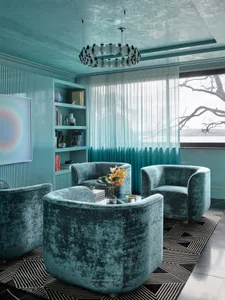 A modern industrial living room with blue upholstered chairs, a black and white geometric rug, and a bookshelf filled with bo