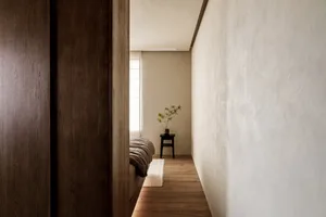 A minimalist bedroom featuring solid wood furniture and a natural plant on a small table.