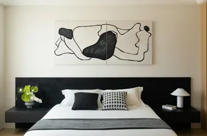 A minimalist bedroom with a textured wooden headboard and white bedding. A black and white abstract painting hangs above the 