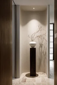 Ceramic vase with dried branches on a wooden pedestal in a minimalist interior design space.